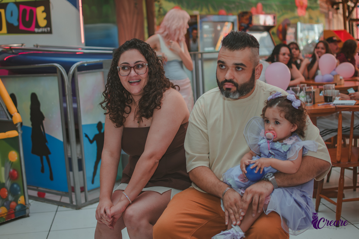 Uma mulher e um homem com bebê no colo, durante retrospectiva em aniversário de 1 ano.