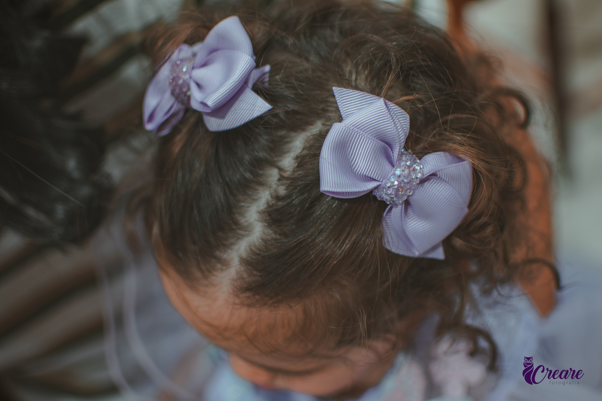 Detalhes dos lacinhos roxo no cabelo de uma menina de 1 ano.
