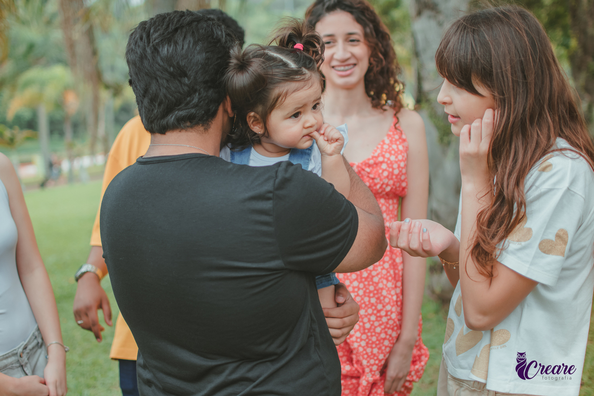 Uma bebê cercada de pessoa, durante sua festa de aniversário de 1 ano no Parque Central de Santo André.