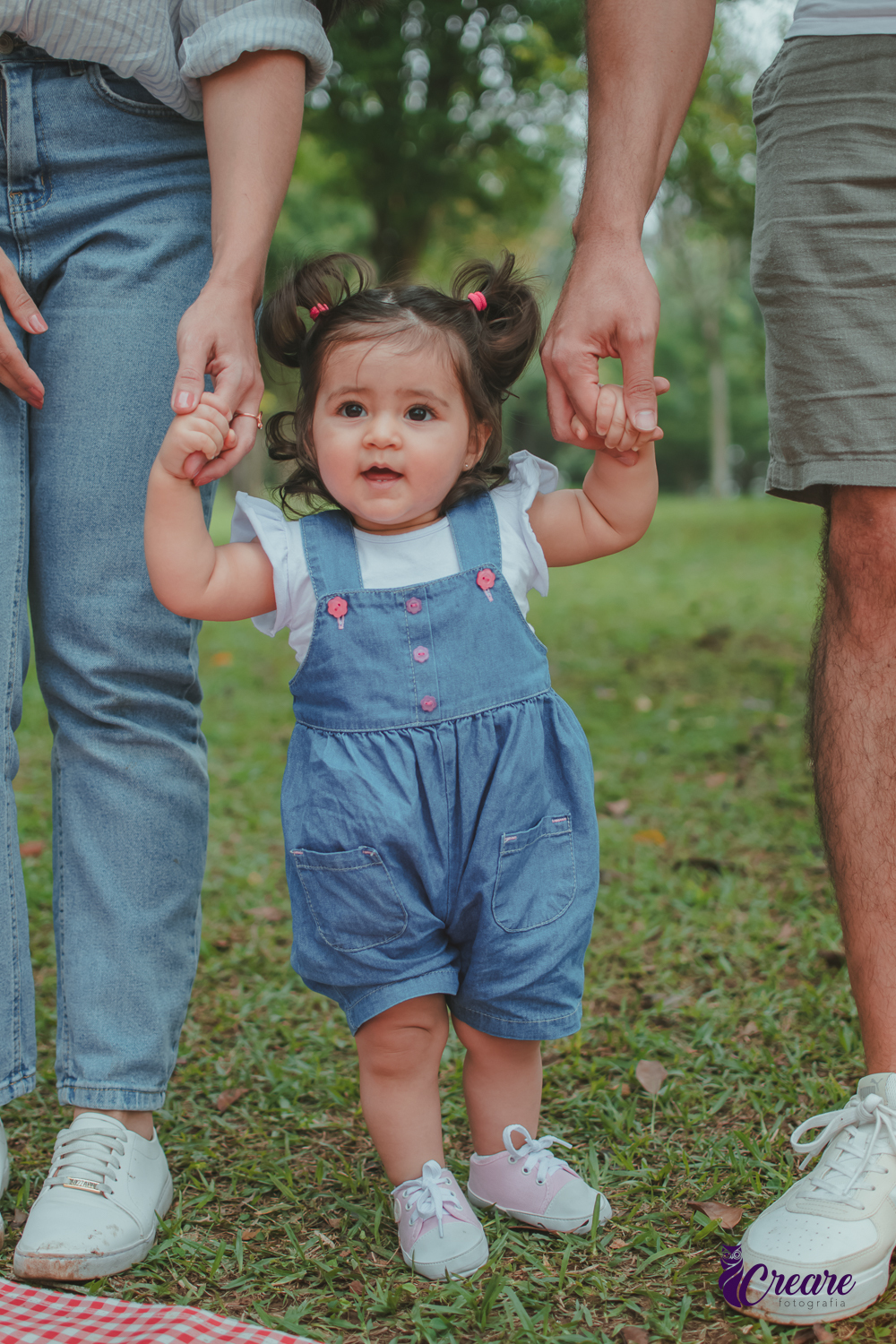 Uma bebê segurando a mão dos seus pais, durante festa de aniversário de 1 ano no Parque Central de Santo André.