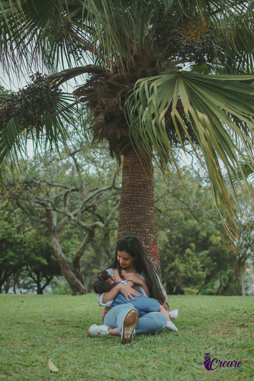 Uma mulher amamentando uma bebê em baixo de uma árvore, durante festa de aniversário de 1 ano no Parque Central de Santo André