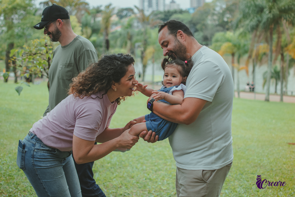 Homem segurando uma bebê no colo enquanto uma mulher brinca com ela durante a comemoração de seu primeiro aniversário no Parque Central de Santo André.