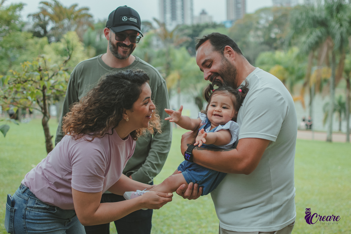 Homem segurando uma bebê no colo enquanto uma mulher brinca com ela durante a comemoração de seu primeiro aniversário no Parque Central de Santo André.