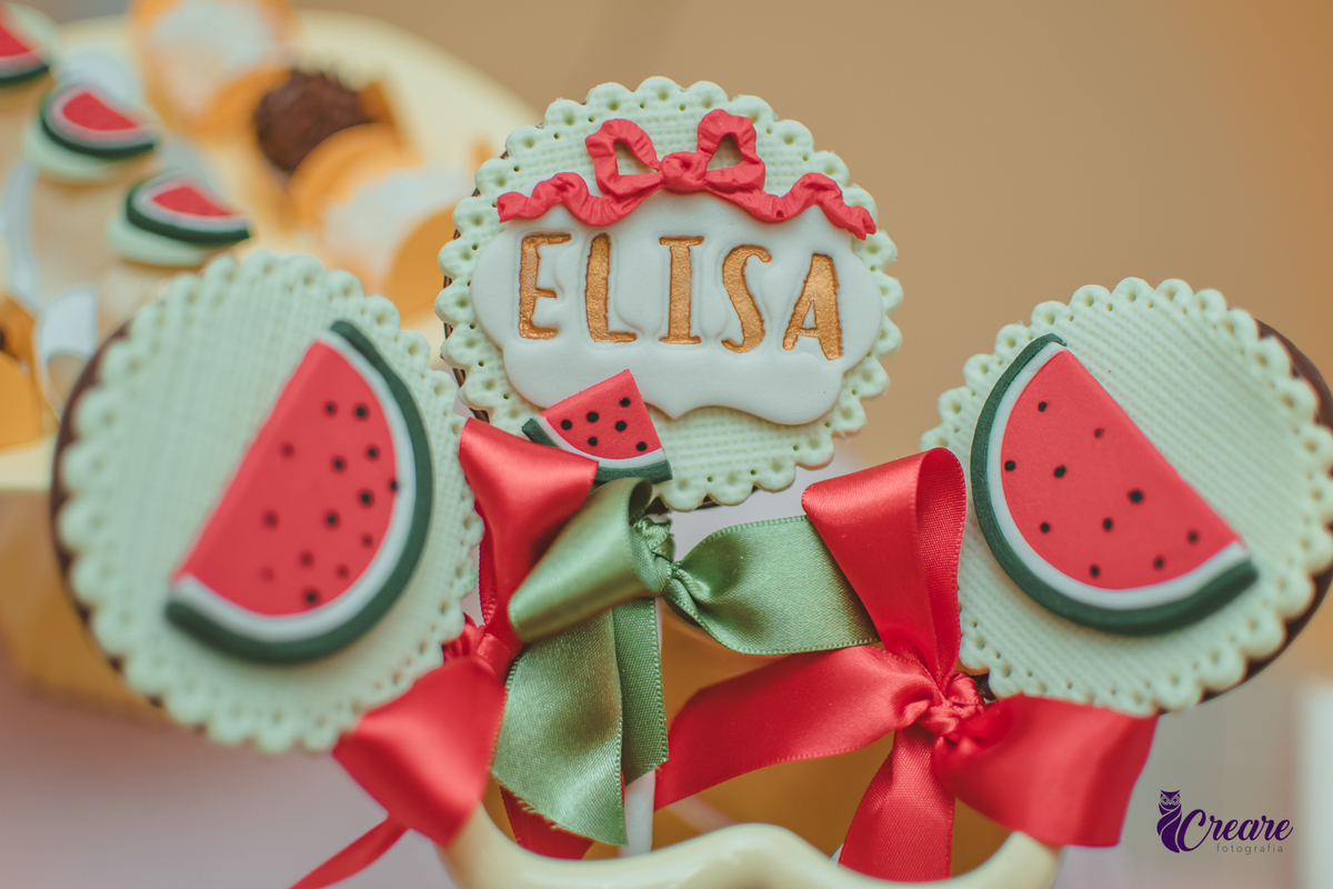 Docinho de aniversário decorado com uma melância aberta e outro com o nome Elisa, para festa de aniversário de 1 ano em casa.