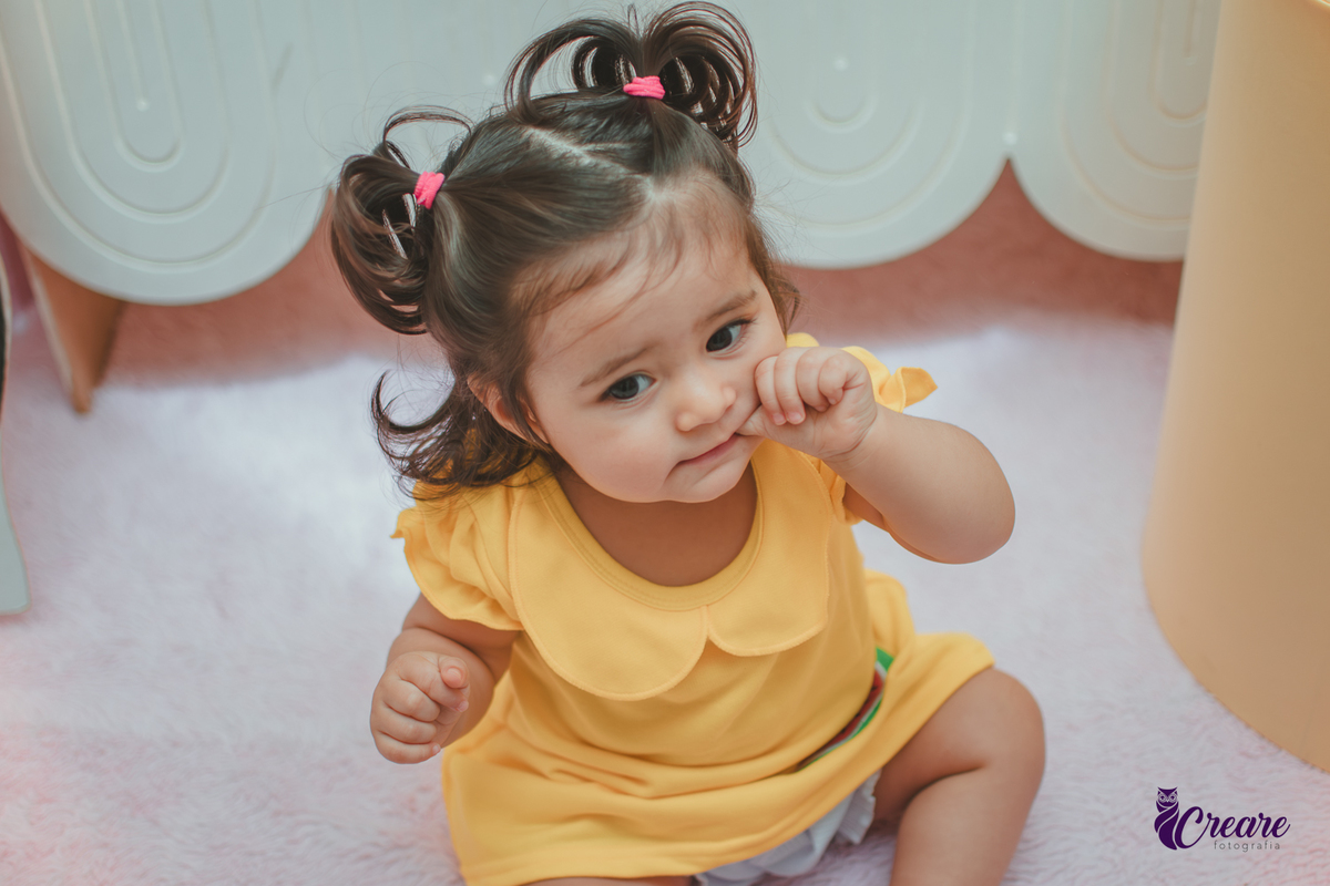Menina de vestido amarelo em frente à decoração de aniversário de 1 ano com tema Magali, em uma festa infantil.