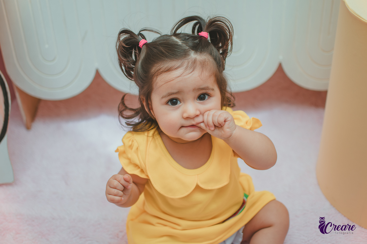 Menina de vestido amarelo em frente à decoração de aniversário de 1 ano com tema Magali, em uma festa infantil.