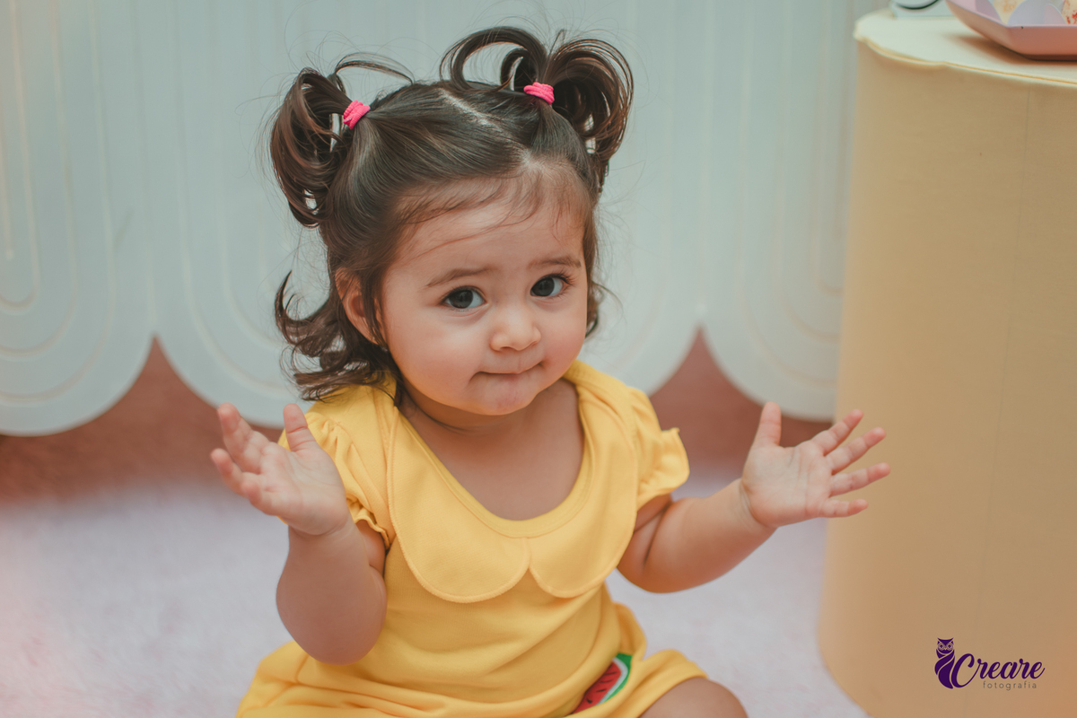 Menina de vestido amarelo em frente à decoração de aniversário de 1 ano com tema Magali, em uma festa infantil.