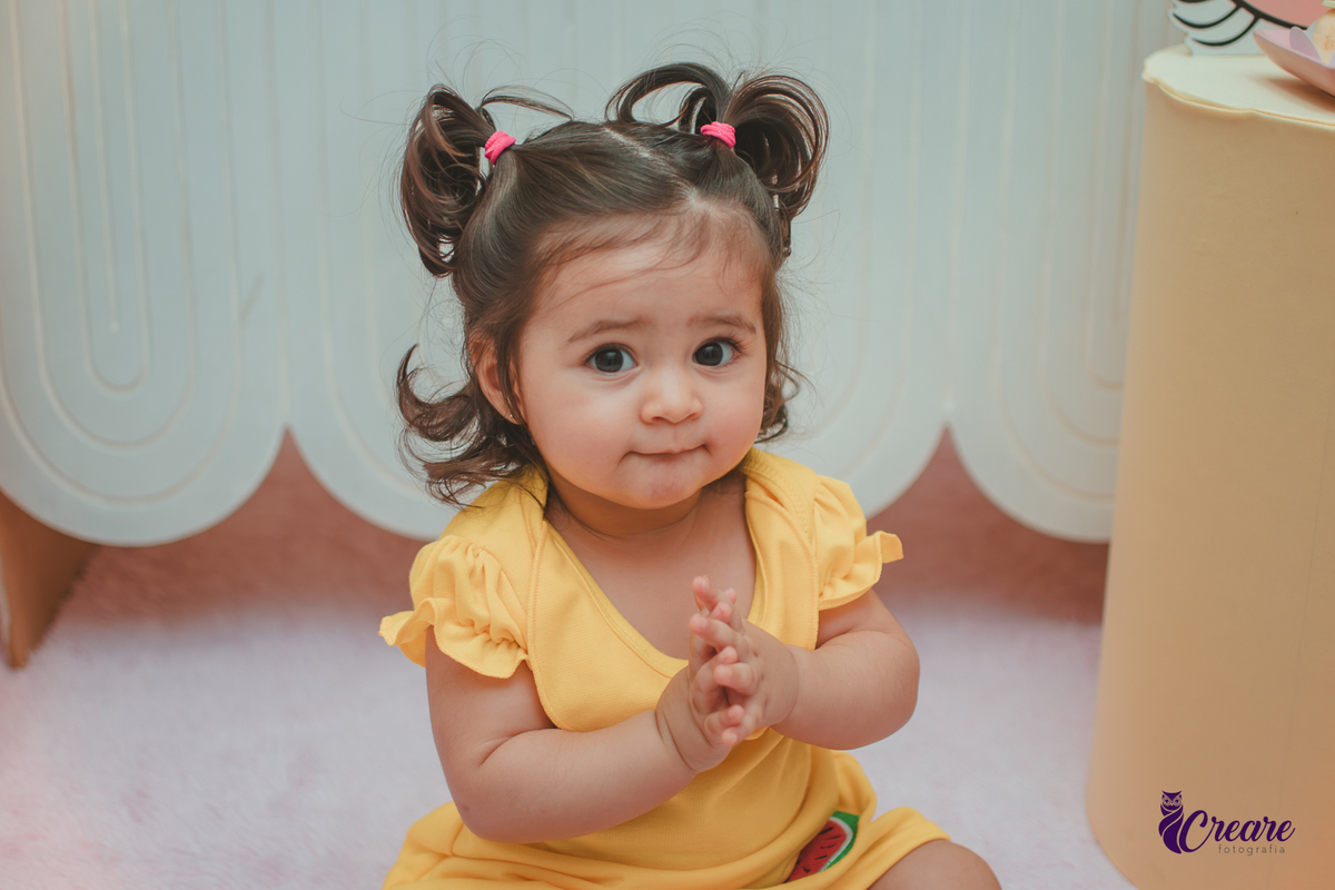 Menina de vestido amarelo em frente à decoração de aniversário de 1 ano com tema Magali, em uma festa infantil.