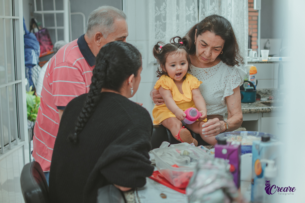 Família reunida na cozinha de casa, brincando com uma bebê de 1 ano durante a comemoração de seu aniversário infantil em casa.