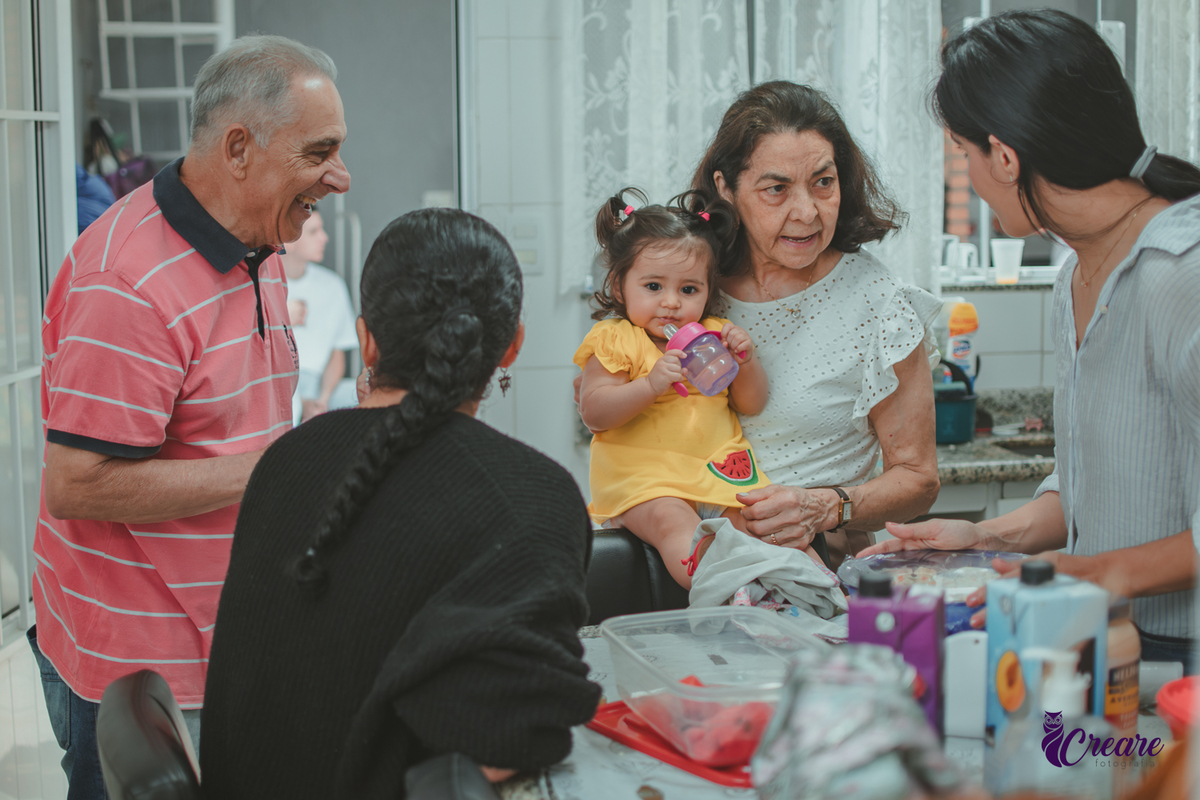 Família reunida na cozinha de casa, brincando com uma bebê de 1 ano durante a comemoração de seu aniversário infantil em casa.