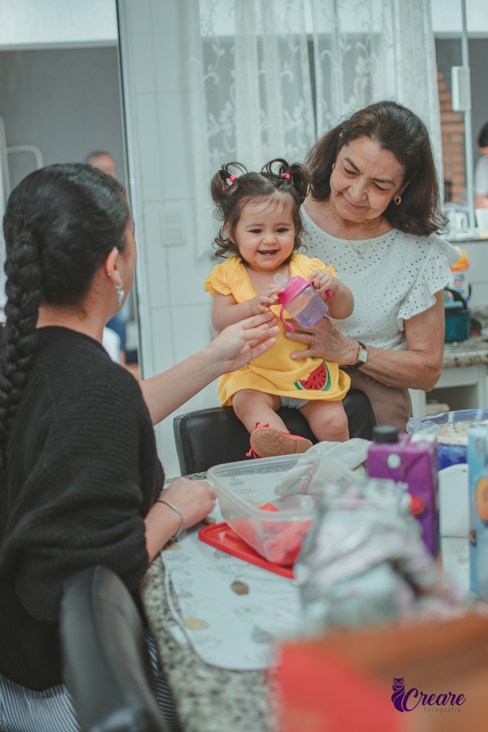Família reunida na cozinha de casa, brincando com uma bebê de 1 ano durante a comemoração de seu aniversário infantil em casa.
