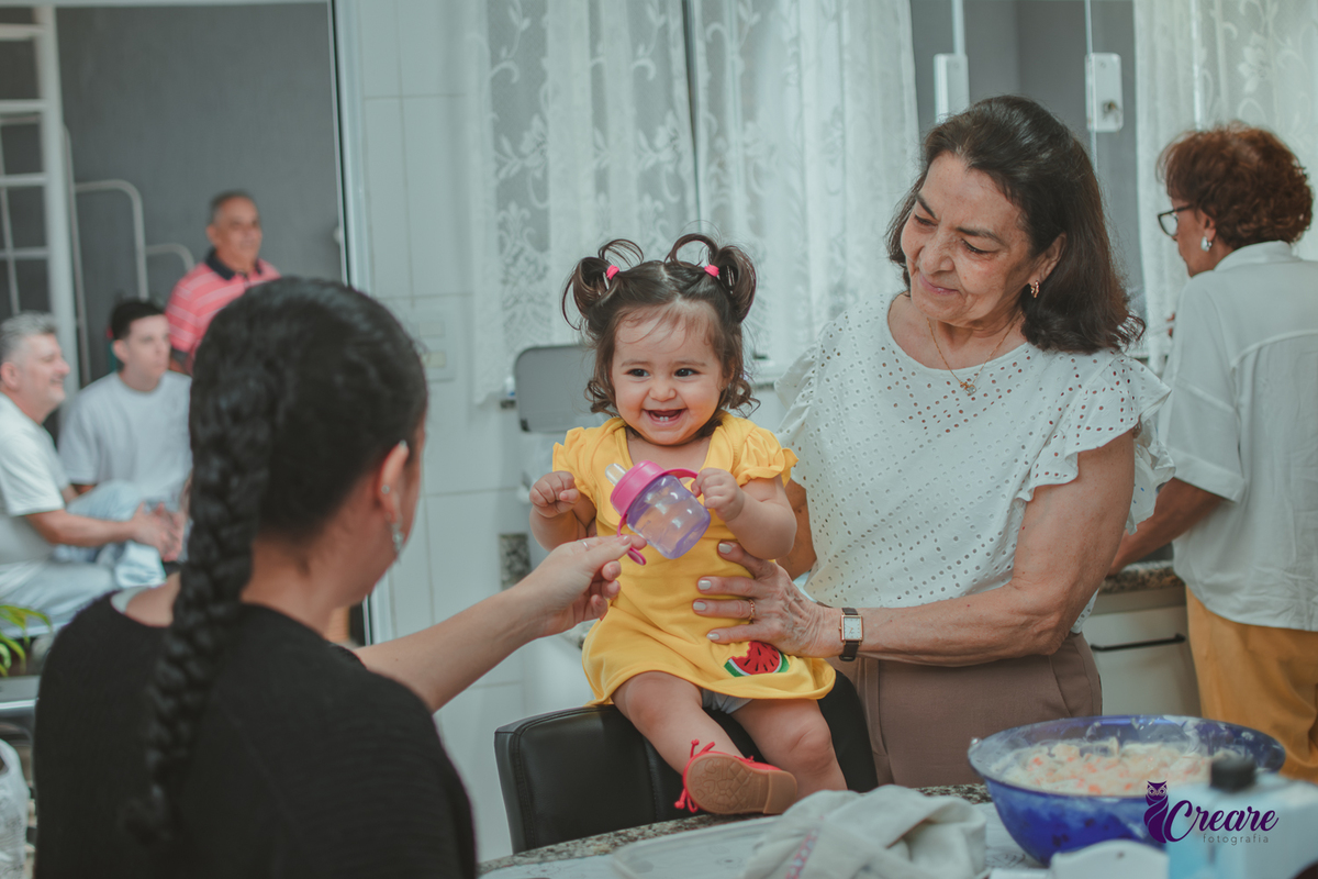 Família reunida na cozinha de casa, brincando com uma bebê de 1 ano durante a comemoração de seu aniversário infantil em casa.