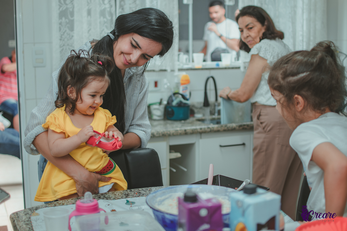 uma mulhere e uma crinaça, dando comida para uma bebê, durante festa de aniversário em casa.