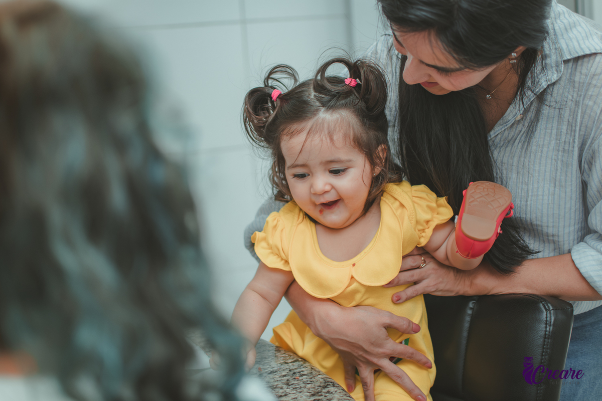 Uma bebê sorrindo enquanto come, durante festa de aniversário de 1 ano em casa.