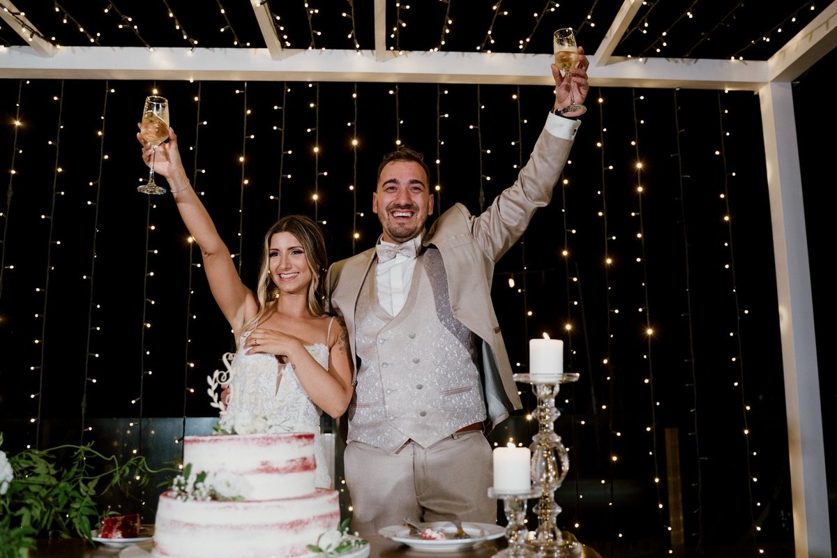 noivos no corte do bolo com copo de champagne a rir