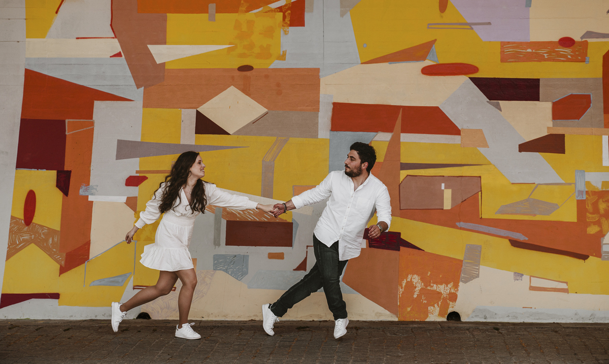 Sessão de solteiros da Sílvia e do Bernardo nas ruas  do Porto na Boavista, com fundo de grafiti amarelo e vermelho, casal a correr divertido, alegre e sorridente, noivo a puxar a noiva.