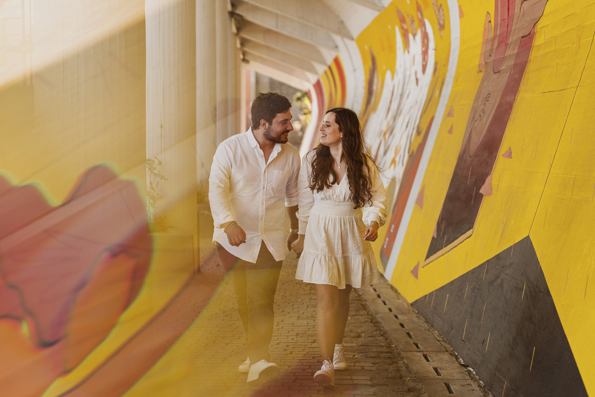 Sessão de solteiros da Sílvia e do Bernardo nas ruas  do Porto na Boavista, com fundo de grafiti amarelo e vermelho e reflexos de prisma óptico.