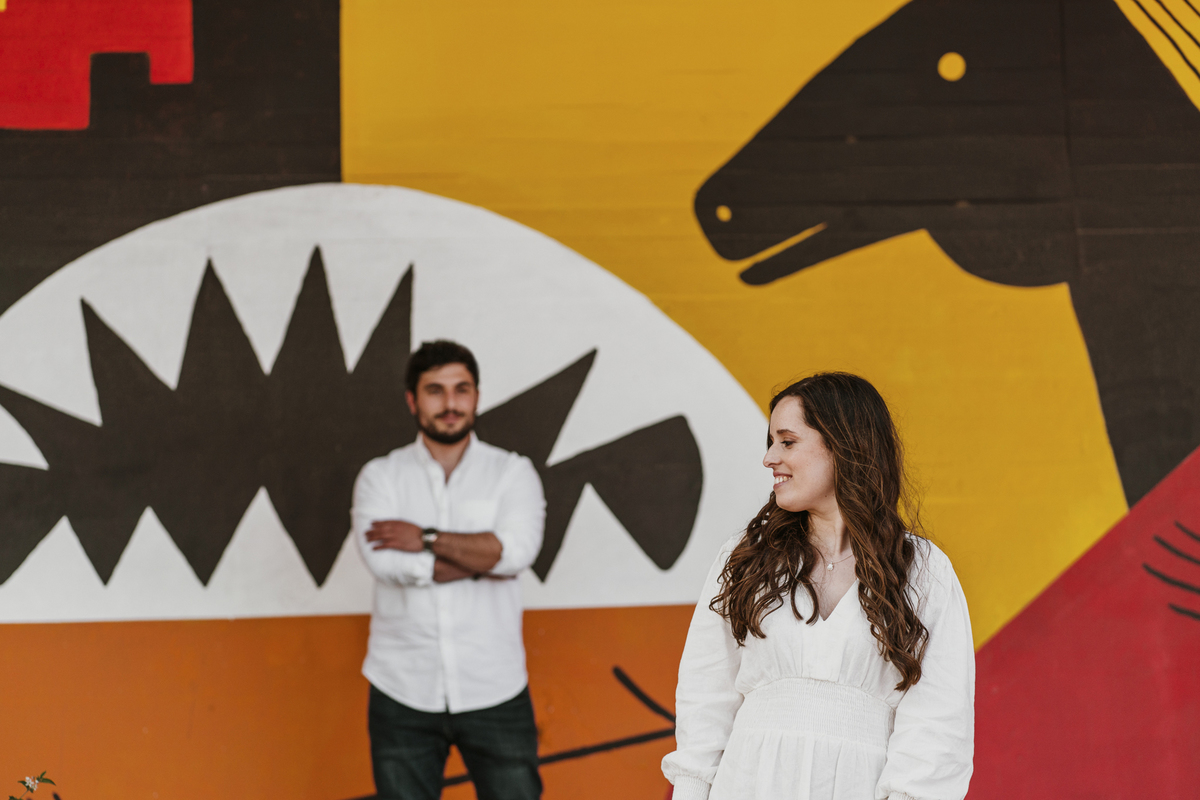 Sessão de solteiros da Sílvia e do Bernardo nas ruas  do Porto na Boavista, com fundo de grafiti amarelo e vermelho e reflexos de prisma óptico, fundo com formas de desenhos geométricos.