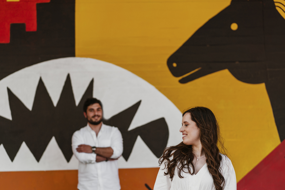 Sessão de solteiros da Sílvia e do Bernardo nas ruas  do Porto na Boavista, com fundo de grafiti amarelo e vermelho e reflexos de prisma óptico, fundo com formas de desenhos geométricos.