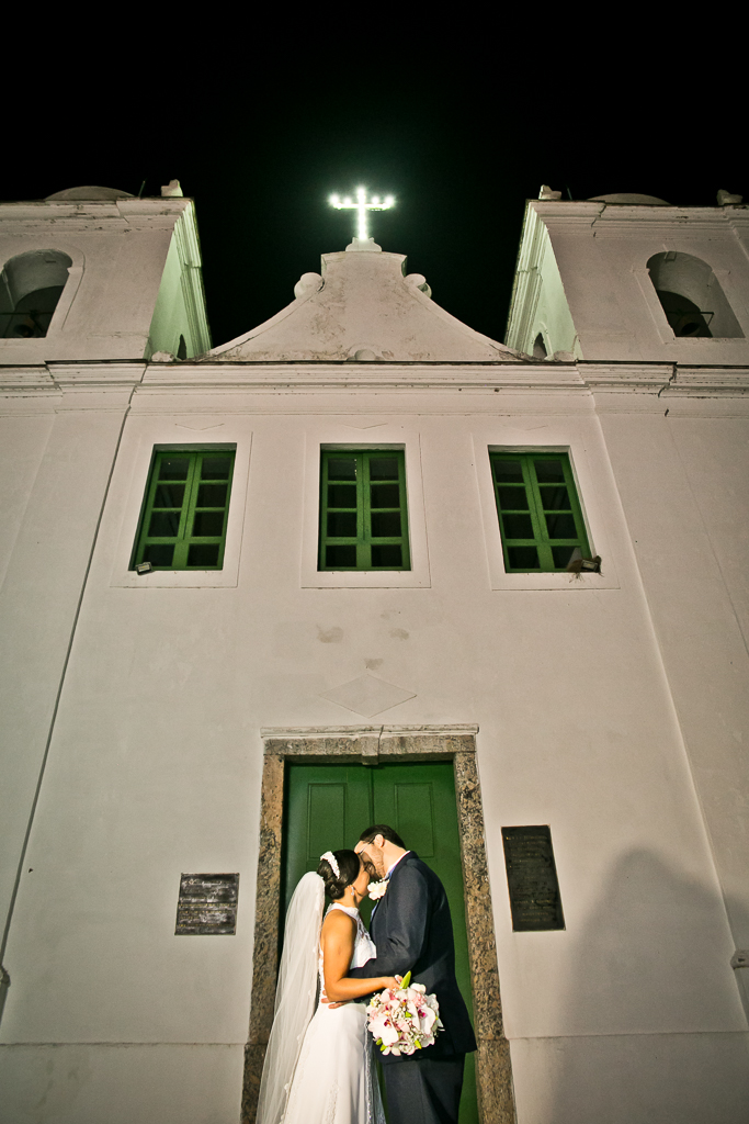 Noivos se beijando em frente a igreja de itaipu onde ocorreu o casamento em fotografia de Mariana Seelinger Fotógrafa de Casamentos em Niterói e RJ