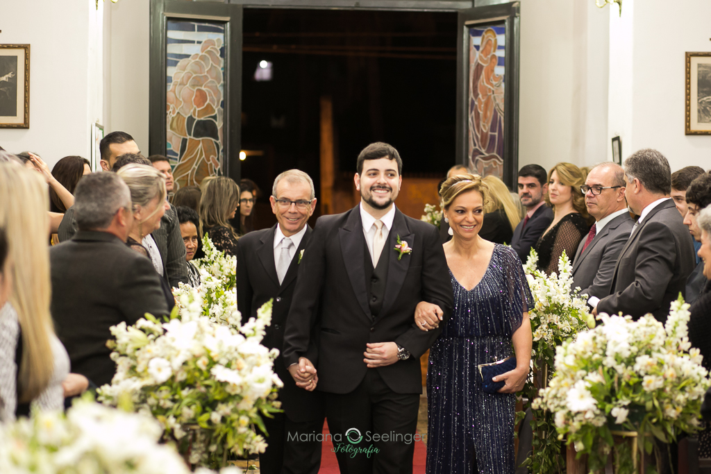 noivo entre os pais em entrada naigreja durante a cerimônia de casamento em fotografia de Mariana Seelinger fotógrafa de casamentos e famílias em Niterói RJ