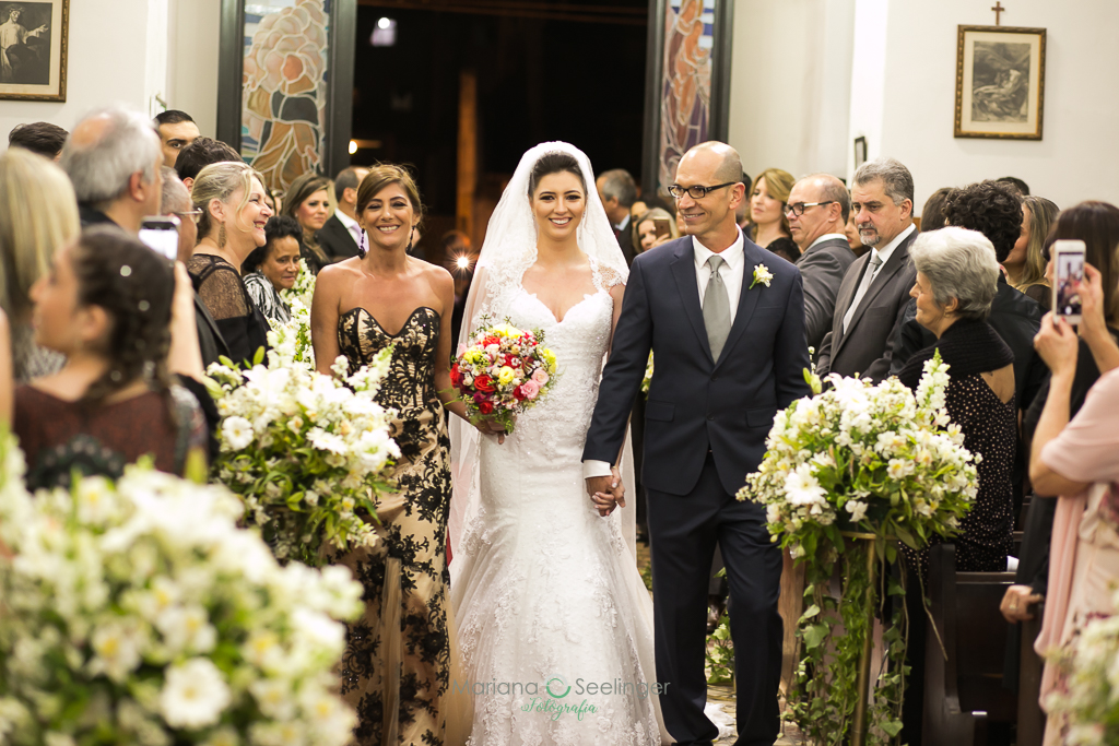 noiva entre ospais em sua entrada naigreja durante a cerimônia de casamento em fotografia de Mariana Seelinger fotógrafa de casamentos e famílias em Niterói RJ