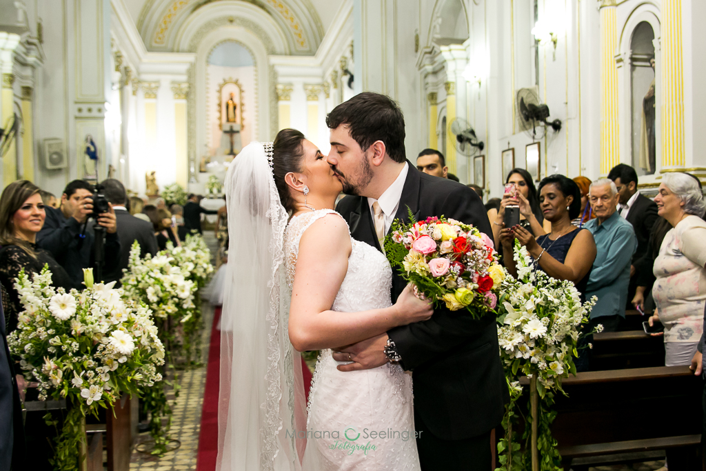 Noivo e noiva se beijando na saída do altar em fotografia de Mariana Seelinger Fotógrafa de Casamentos em Niterói e RJ