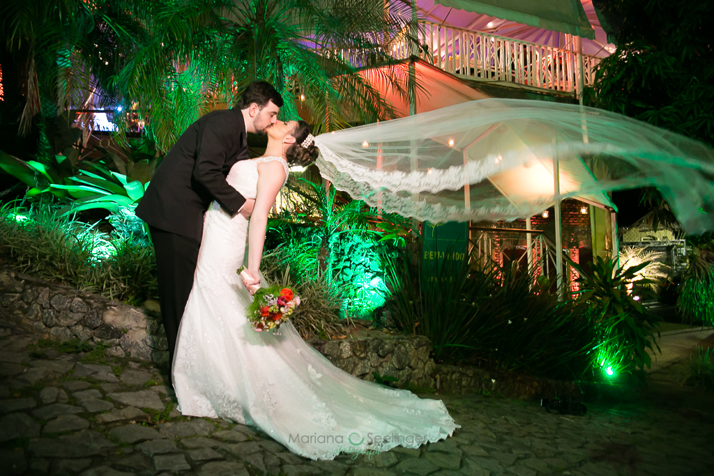 Noivo e noiva se beijando com o véu da noiva voando em fotografia de Mariana Seelinger Fotógrafa de Casamentos em Niterói e RJ