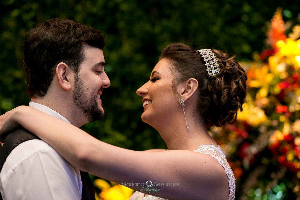 Foto da noiva e do noivo abraçados com o fundo de flores em fotografia de Mariana Seelinger Fotógrafa de Casamentos em Niterói e RJ