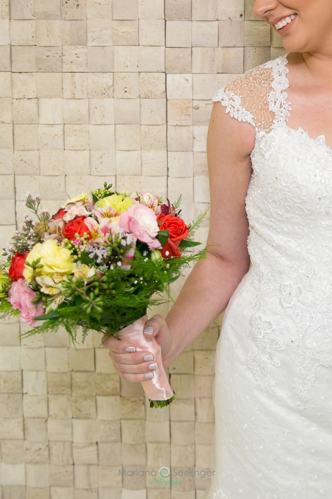noiva olhando ao bouquet de flores coloridas e vestido de renda vazada emdecotecoração em fotografia de Mariana Seelinger fotógrafa de casamentos e famílias em Niterói RJ