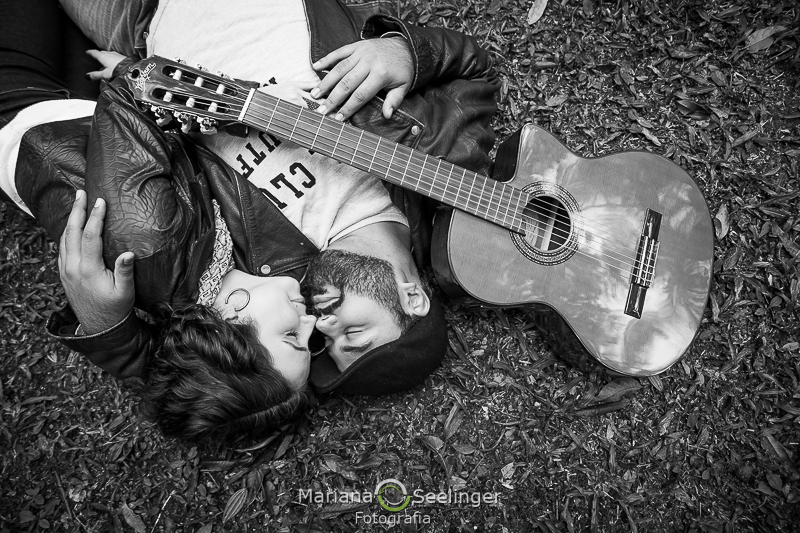 Fotografia em preto e branco do casal na grama deitados com o violão apoiado no noivo em ensaio de casal em Teresópolis - RJ por Mariana Seelinger Fotografia