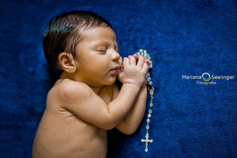 Gael com um terço azul enrolado nas mãozinhas em ensaio newborn