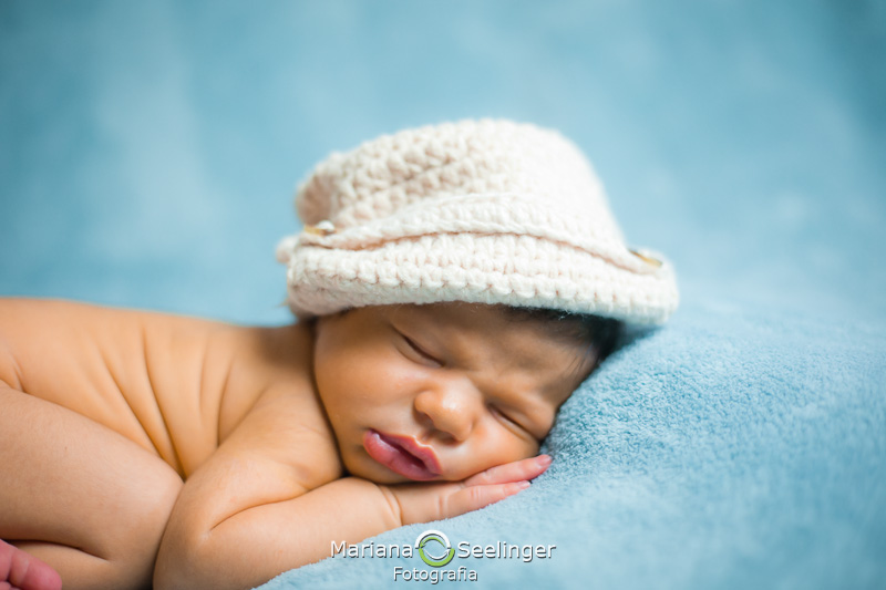 Deitado num cobertor azul de chapéu de croché branco Gael posa em seu ensaio newborn