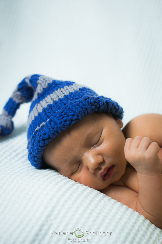 Deitado de touquinha azul e cinza por fotográfa Mariana Seelinger em ensaio newborn em Niterói - RJ