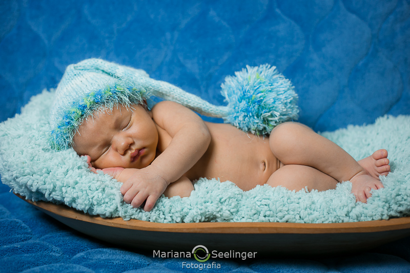 deitado numa pequena barquinha com touquinha de tricô azul em ensaio newborn por Mariana Seelinger Fotografia