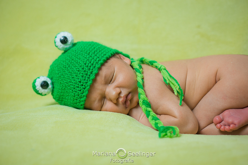 Deitado em cobertor verde de touca de tricô de sapinho em ensaio recém nascido em Niterói RJ por Mariana Seelinger Fotografia