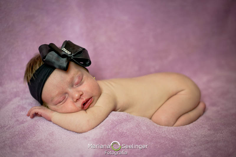 bebê de tiara de lacinho preto em manta rosa em ensaio newborn