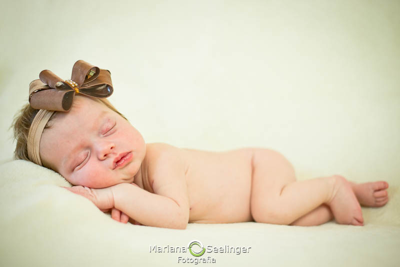 com tiara de lacinho marrom a pequena Maria Antonia deitada em pose newborn para ensaio de Mariana Seelinger Fotografia em Niterói -RJ