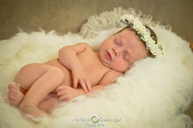 bebê com coroa de flores brancas deitada em tapete felpudo branco em ensaio newborn em Niterói - RJ por Mariana Seelinger Fotografia