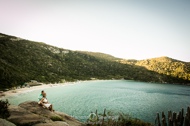 o casal em cima da pedra olhando o mar cristalino de Arraial do Cabo - RJ em ensaio por Mariana Seelinger Fotografia
