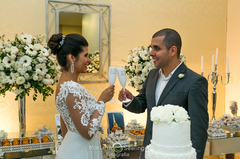 o brinde dos noivos sorridentes ao lado do bolo no casamento no Rio de Janeiro -RJ