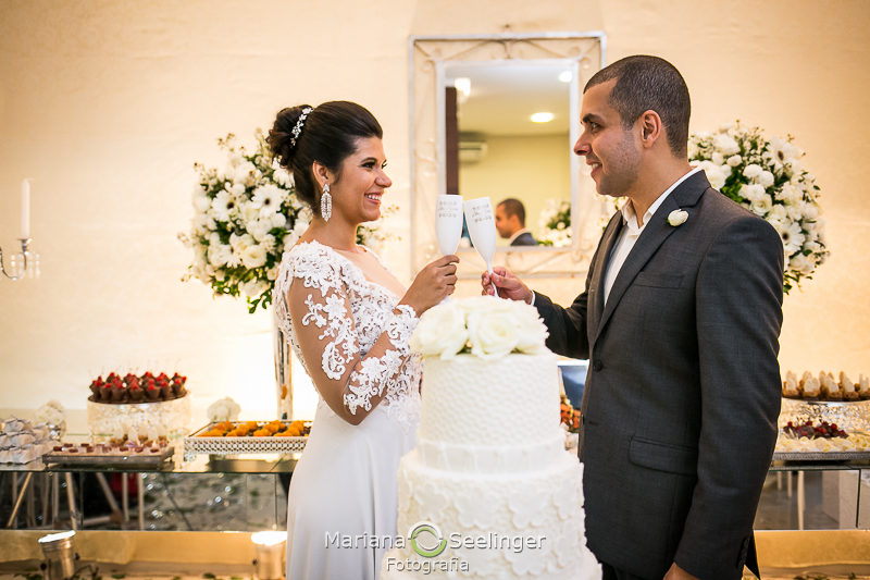 os noivos brindam diante do bolo de casamento em Rio de Janeiro - RJ por Mariana Seelinger Fotografia