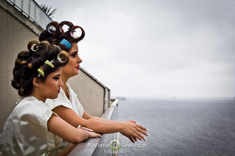 a noiva e sua filha de bobs nos cabelos olhando o mar em fotografia por Mariana Seelinger