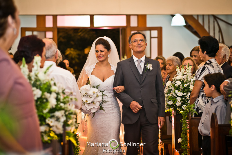 a noiva e o pai pelo corredor da igreja em fotografia por Mariana Seelinger Fotografia em Niterói - RJ