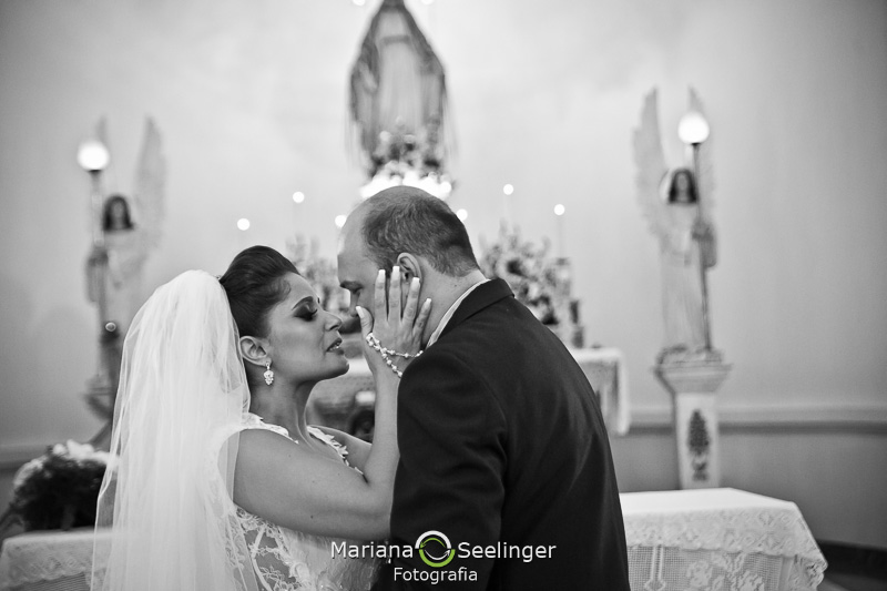 a noiva segura o rosto do noivo diante do altar em casamento em Niterói - RJ