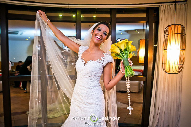 a noiva estende o seu véu com uma mão e segura o buquê amarelo e o terço na outra em fotografia por Mariana Seelinger