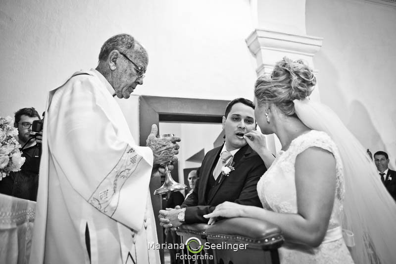 Foto em preto e branco do noivo recebendo hóstia da noiva em casamento registrado por Mariana Seelinger Fotografia de Casamentos e Familias em Niterói RJ