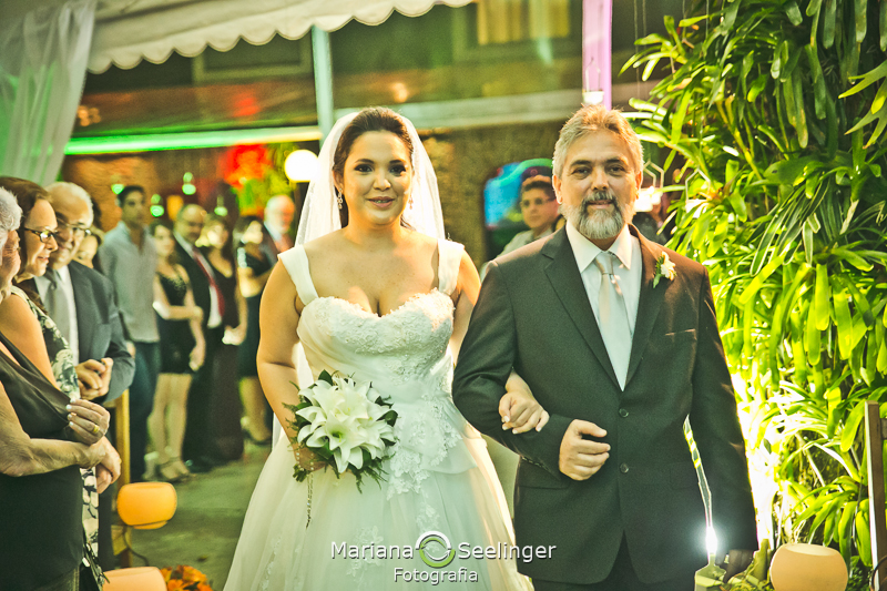 Noiva emocionada acompanhada pelo pai a caminnho do altar em casamento registrado por Mariana Seelinger Fotografia de Casamentos e Familias em Niterói RJ