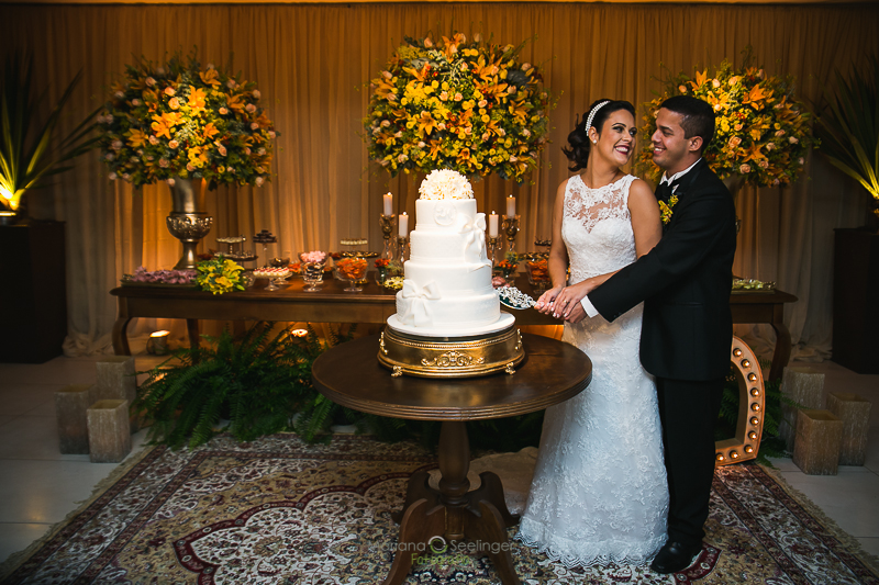 Noivos cortando bolo de 4 andares em mesa redonda em casamento registrado por Mariana Seelinger Fotografia de Casamentos e Familias em Niterói RJ