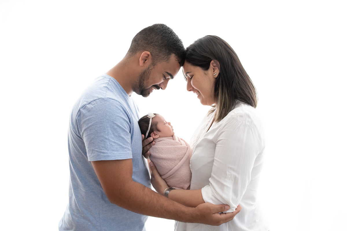 Pais abraçam bebê em ensaio newborn, foto em contra luz